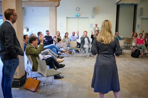 Deelnemers steken hun hand op tijdens een vraag in de zaal