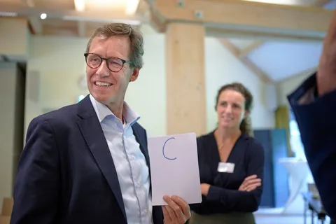 Man lacht en houdt een kaartje met de letter C omhoog tijdens de quiz