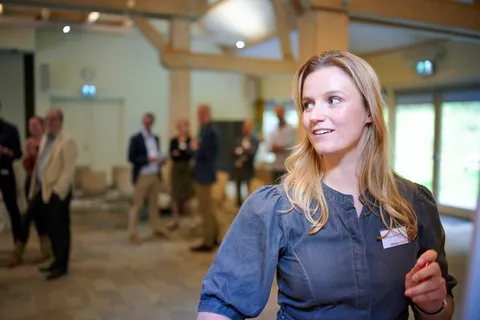 Vrouw met naamkaartje kijkt opzij, op de achtergrond staan deelnemers na te praten
