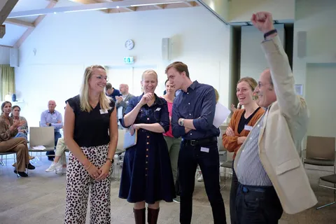 Deelnemers klappen en juichen, een man balt triomfantelijk zijn vuist tijdens de quiz