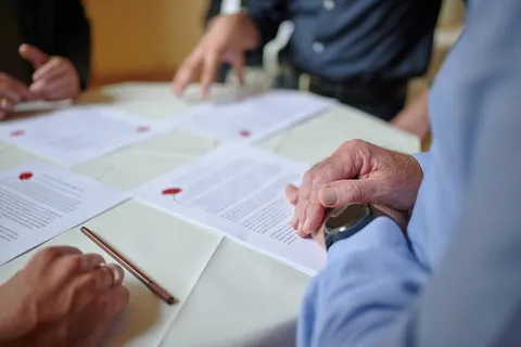 Deelnemers wijzen op documenten met rode zegelstempels op een tafel