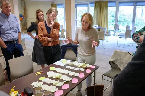 Vrouw licht memoblaadjes op tafel toe aan luisterende deelnemers