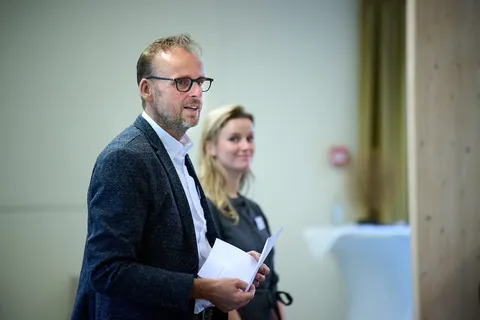 Man met bril spreekt, een vrouw luistert naast hem
