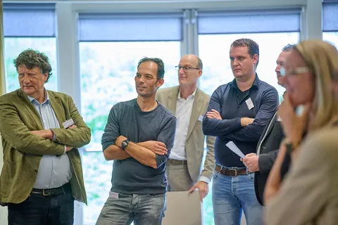 Deelnemers staan met over elkaar geslagen armen te luisteren naar een gesprek