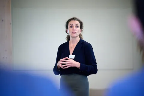 Spreekster met samengevouwen handen richt zich tot het publiek