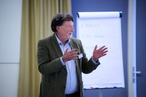 Man met krullend haar spreekt gebarend voor een flipover