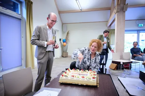 Man met champagneglas kijkt toe terwijl een vrouw met rood haar de taart aansnijdt