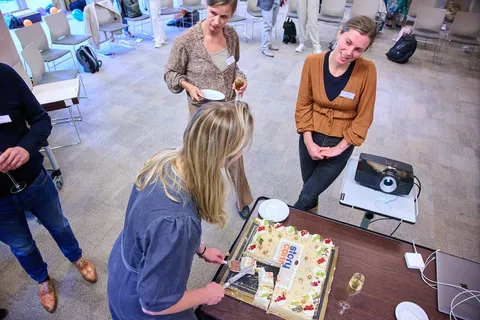 Vrouw snijdt de taart met het StoryConnect-logo aan, collega's kijken toe met een glas champagne