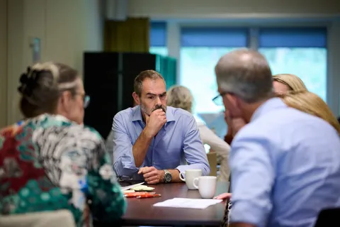 Deelnemers luisteren geconcentreerd aan tafel tijdens een gesprek