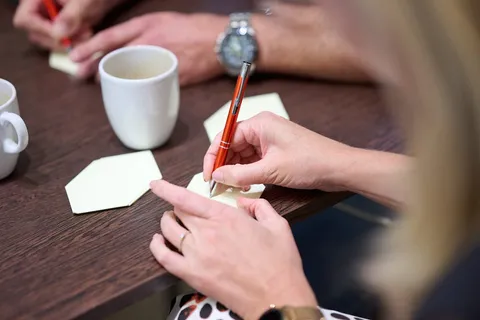 Deelnemers schrijven met een pen op gele memoblaadjes op tafel