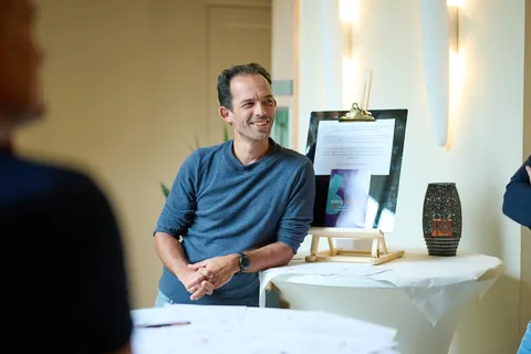 Man leunt glimlachend tegen een tafel met een tekstbord over storytelling