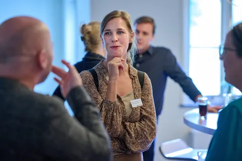 Vrouw gebaart pratend in een groepje tijdens de borrel
